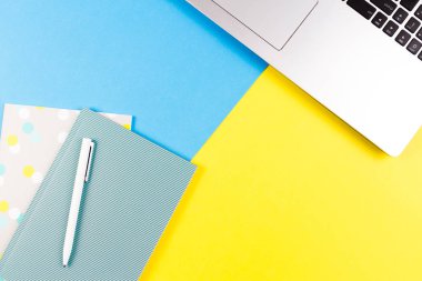 Mavi ve sarı renk arka plan üzerinde dizüstü bilgisayar, kağıt defter ve beyaz kalem Üstten Görünüm