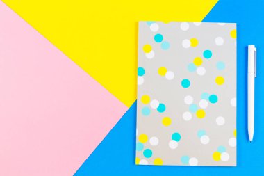 Mavi, sarı ve pembe arka plan üzerinde kağıt defter kalem ile Üstten Görünüm.