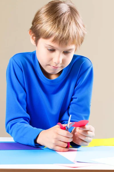 Schoolboy cortando papel colorido com tesoura na mesa — Fotografia de Stock