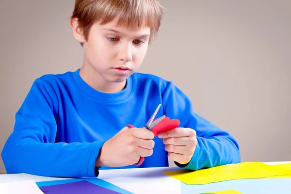 Criança cortando papel colorido com tesoura na mesa — Fotografia de Stock