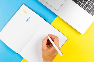 Kadın el not defterinde mavi ve sarı arka plan üzerinde yazma. Üstten Görünüm