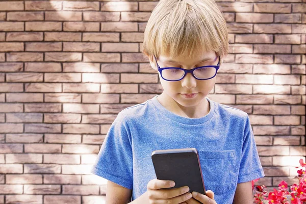 Menino com óculos usando telefone celular ao ar livre . — Fotografia de Stock