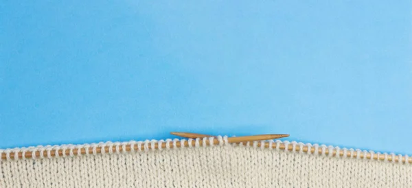 Top view of knitting with two bamboo knitting needles on blue background — Stock Photo, Image