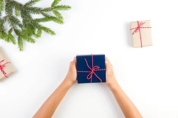 Bovenaanzicht van kid handen met een cadeautje. Geschenkdozen verpakt in ambachtelijke papier en christmas tree branch op witte achtergrond — Stockfoto