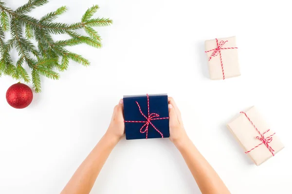 Karácsonyi háttér a gyerek kezében tartja a jelen box, kis díszdobozok csomagolva kézműves papír és a karácsonyfa ága és dekoráció fehér háttér — Stock Fotó