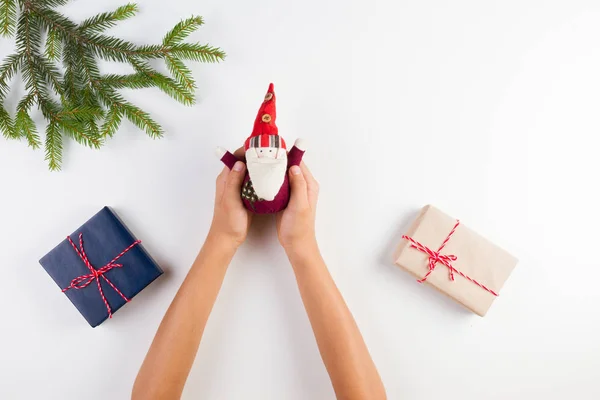 Szemközti nézet a gyerek kezei karácsonyi dekoráció. Ajándék dobozok és a karácsony fa ága, a fehér asztal — Stock Fotó