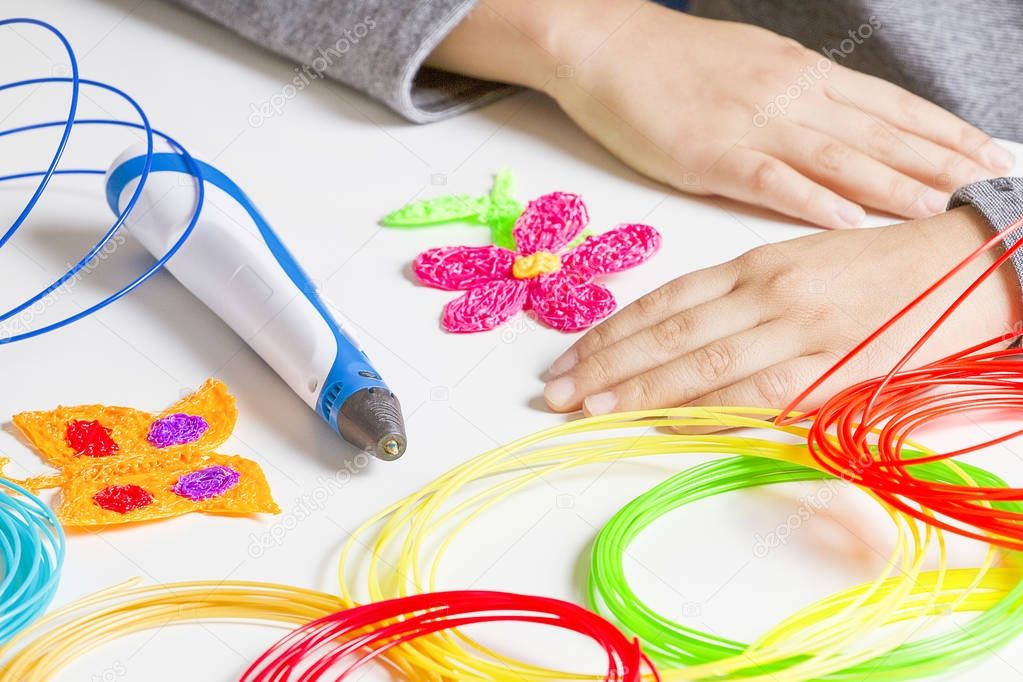 Kid hands and 3d printing pen, colorful filaments on white desk.