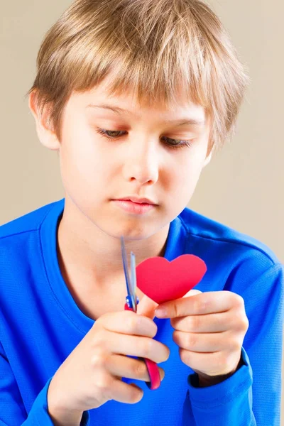 Menino cortando coração de papel vermelho com tesoura — Fotografia de Stock