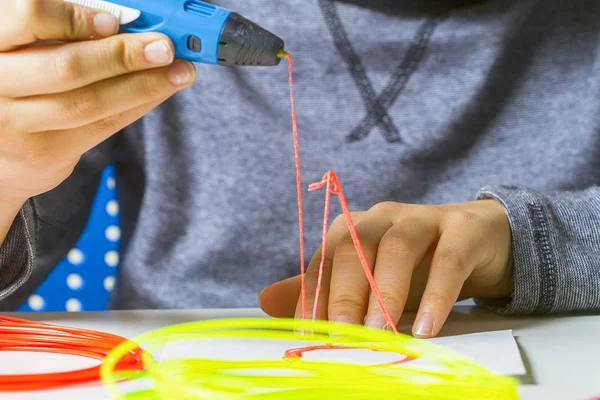 Manos de niño con lápiz de impresión 3D, filamentos de colores en el escritorio blanco . — Foto de Stock