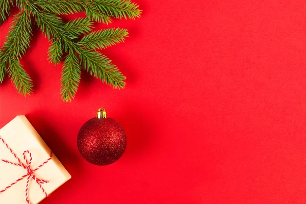 Karácsonyi összetétele vörös háttérben. Zöld fenyő fa ágai, Xmas jelen box és dekoráció. — Stock Fotó