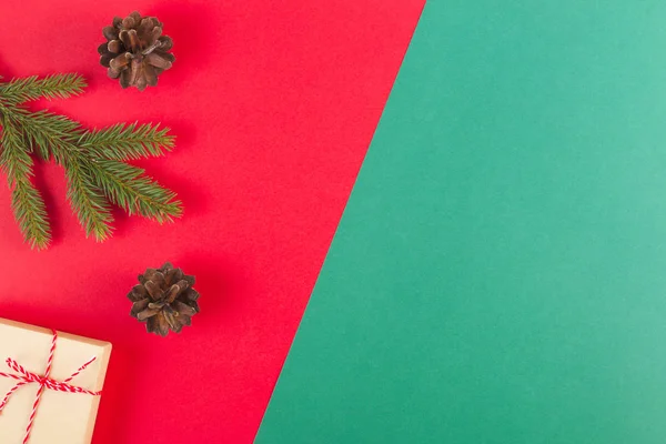 Christmas sammansättning på röd och grön bakgrund. Gröna fir trädgren, kottar och nuvarande box — Stockfoto