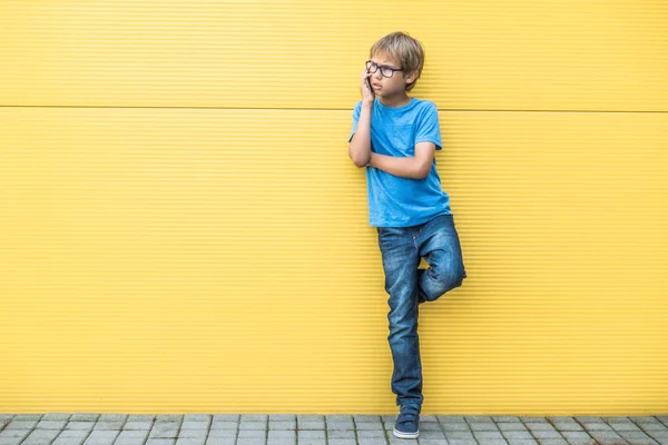 휴대 전화 서 야외에서 노란색 벽 근처에 심각한 작은 소년 — 스톡 사진