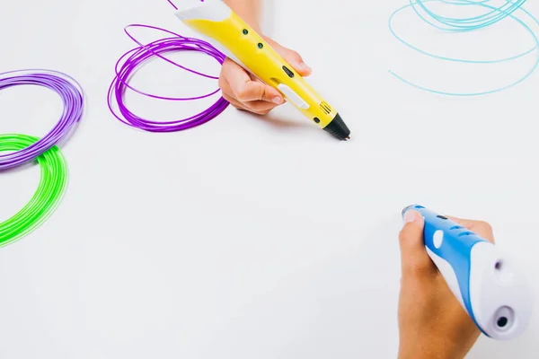 Kids hands holding 3d printing pens with filaments on white background. Top view