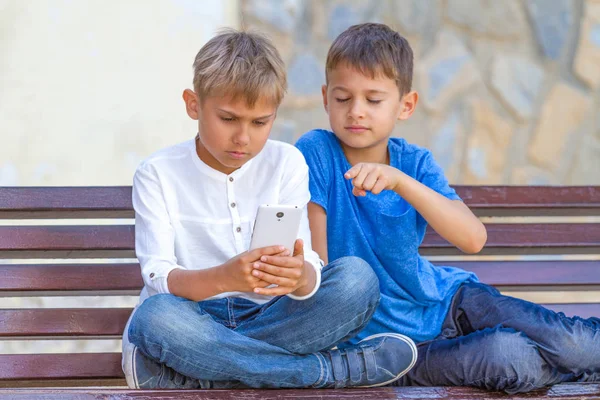 Meninos com telefone celular sentado no banco ao ar livre — Fotografia de Stock