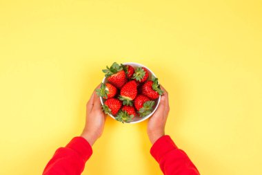 Çocuk el Sarı zemin üzerine taze çilek ile kase tutar
