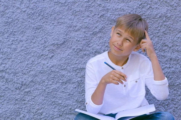 Pojken tänkte med ett finger på pannan. Kid sitter på marken och gör skolan läxor. — Stockfoto