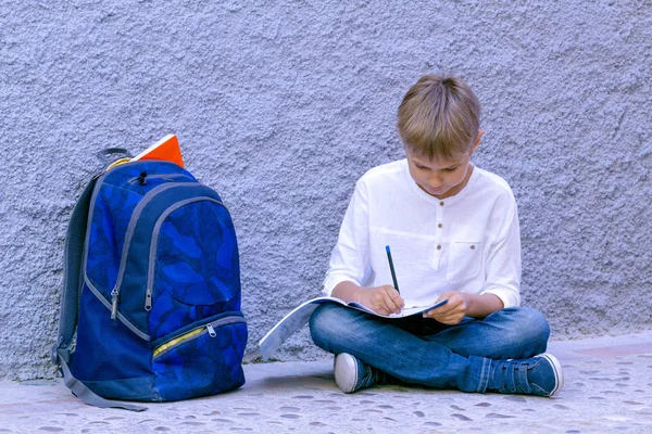 Chico haciendo deberes escolares. Niño leyendo, escribiendo y pensando sentado en el suelo . — Foto de Stock