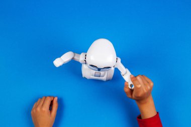 Oyuncak robot üzerinde mavi arka plan ile çocuk el.