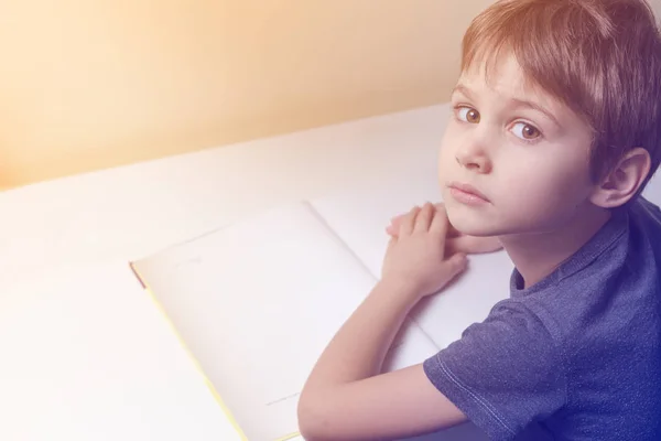 Niño sentado en la mesa, leyendo libro y haciendo su tarea —  Fotos de Stock