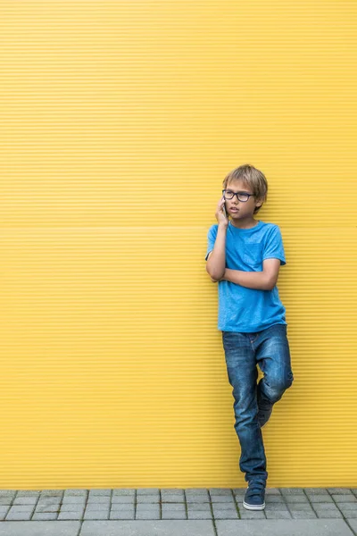 휴대 전화 서 야외에서 노란색 벽 근처에 심각한 작은 소년 — 스톡 사진