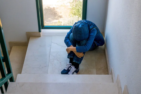 Ledsen pojke sitter ensam i hörnet av en trappa — Stockfoto
