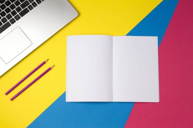 Dizüstü bilgisayar açık defter ve kalemler renkli arka plan üzerinde.