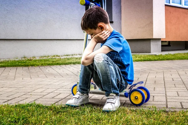 Niño triste molesto sentado en el scooter al aire libre — Foto de Stock