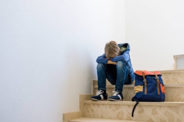 Merdiven köşede tek başına oturmak sırt çantası ile üzgün çocuk