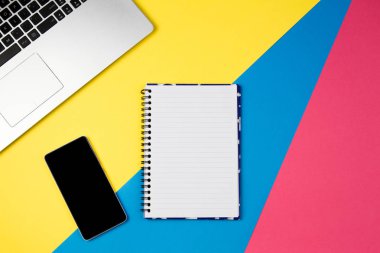 Üstten Görünüm office tablo Resepsiyon. Dizüstü bilgisayar, akıllı telefon ve açık spiral defter sayfası renkli arka plan üzerinde çalışma alanı.