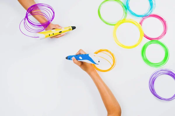 Des mains d'enfants tenant des stylos d'impression 3D avec des filaments sur fond blanc. Vue du dessus — Photo