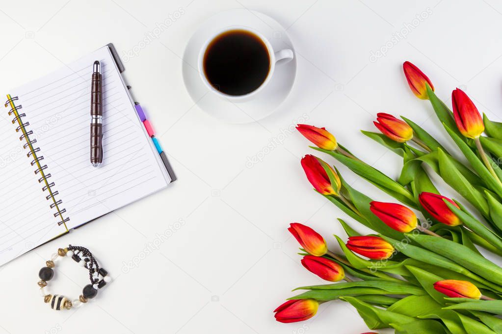 Office desk table with paper notebook, pen, coffee cup and beautiful fresh bunch of flowers tulips