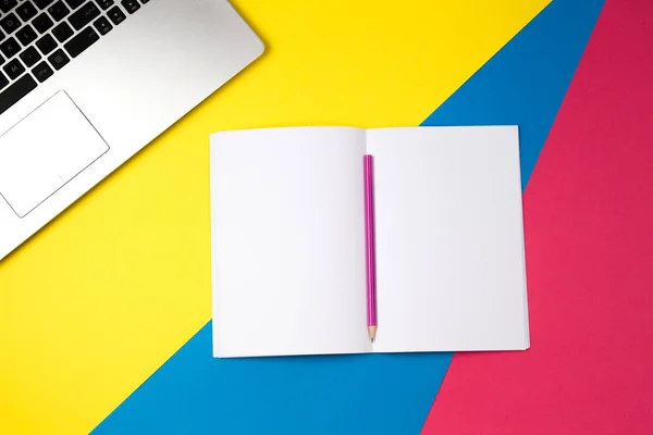 Ovanifrån office bord skrivbord. Arbetsytan med laptop och öppna anteckningsbok med penna på färgstarka bakgrund. — Stockfoto