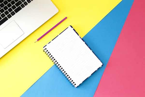 Ovanifrån office bord skrivbord. Arbetsytan med laptop, penna och öppen spiral notebook sida på färgstarka bakgrund. — Stockfoto