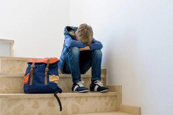 Merdiven köşede tek başına oturmak sırt çantası ile üzgün çocuk