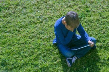 Güneşli bir günde dışarıda çimlere oturup tablet bilgisayar çocukla.