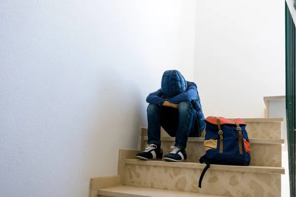 Ledsen pojke med ryggsäck som sitter ensam i hörnet i trappan — Stockfoto