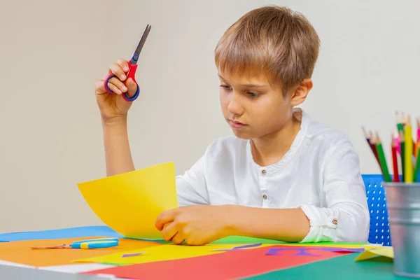 Bambino che taglia carta colorata con le forbici a tavola — Foto Stock