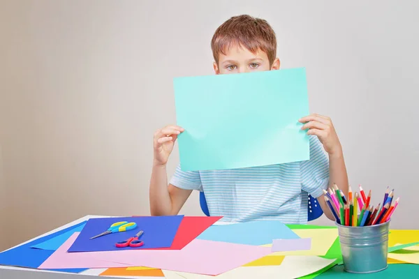 空白の空の色の紙シートを保持している小さな男の子は、顔を覆ってください。. — ストック写真