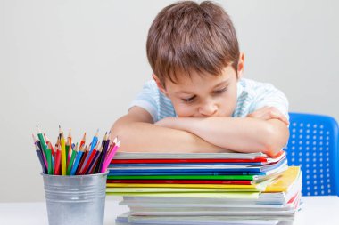 Okul kitapları ve dizüstü bilgisayarlar yığını ile masa başında oturan üzgün okul çocuğu