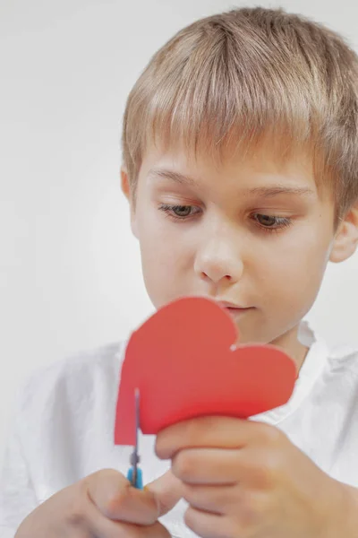 Criança cortando coração de papel vermelho com tesoura — Fotografia de Stock