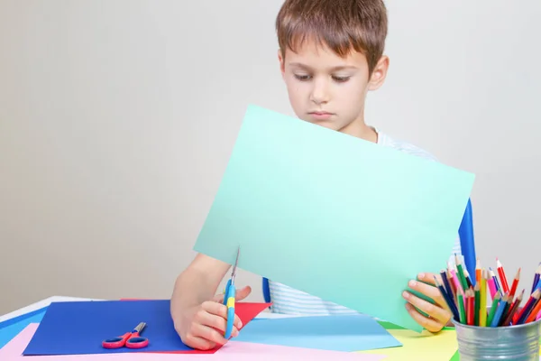 Criança cortando papel colorido com tesoura na mesa — Fotografia de Stock