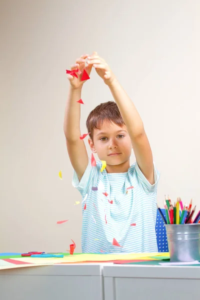 Bambino gettando piccolo pezzo di carta colorata come coriandoli dopo aver creato il biglietto di auguri — Foto Stock