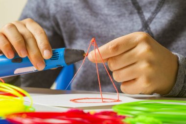 Çocuk elleriyle 3d kalem, beyaz masa üzerinde renkli filamentler.