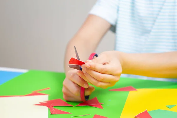 Детские руки режут цветную бумагу ножницами за столом — стоковое фото