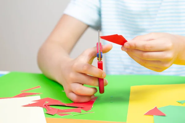 Mãos de criança cortando papel colorido com tesoura na mesa — Fotografia de Stock