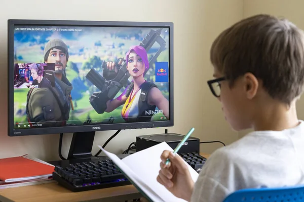 Boy doing homework and watching people play strategy video games and streaming on YouTube. Vilnius, Lithuania - 19 October 2019 — Stock Photo, Image