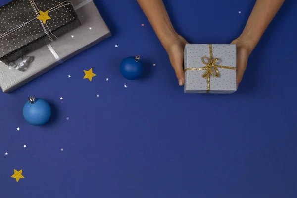 Fondo de Navidad. Vista superior a las manos sosteniendo regalos de Navidad sobre fondo azul con brillantes estrellas de brillo y decoración bauble — Foto de Stock