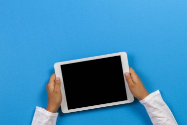 Açık mavi arka plan üzerinde beyaz tablet bilgisayar tutan çocuk el