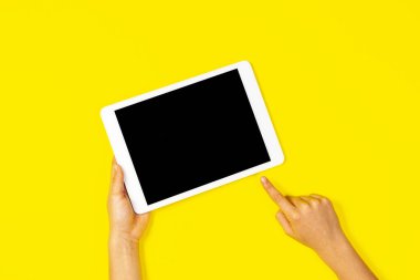 Çocuk elinde beyaz tablet bilgisayarla sarı arkaplanda boş bir ekrana işaret ediyor.