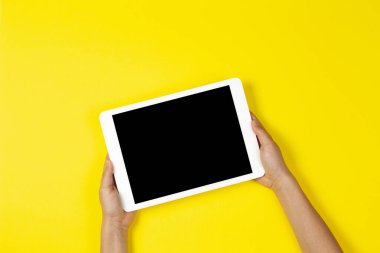 Sarı zemin üzerinde beyaz tablet bilgisayar tutan çocuk elleri